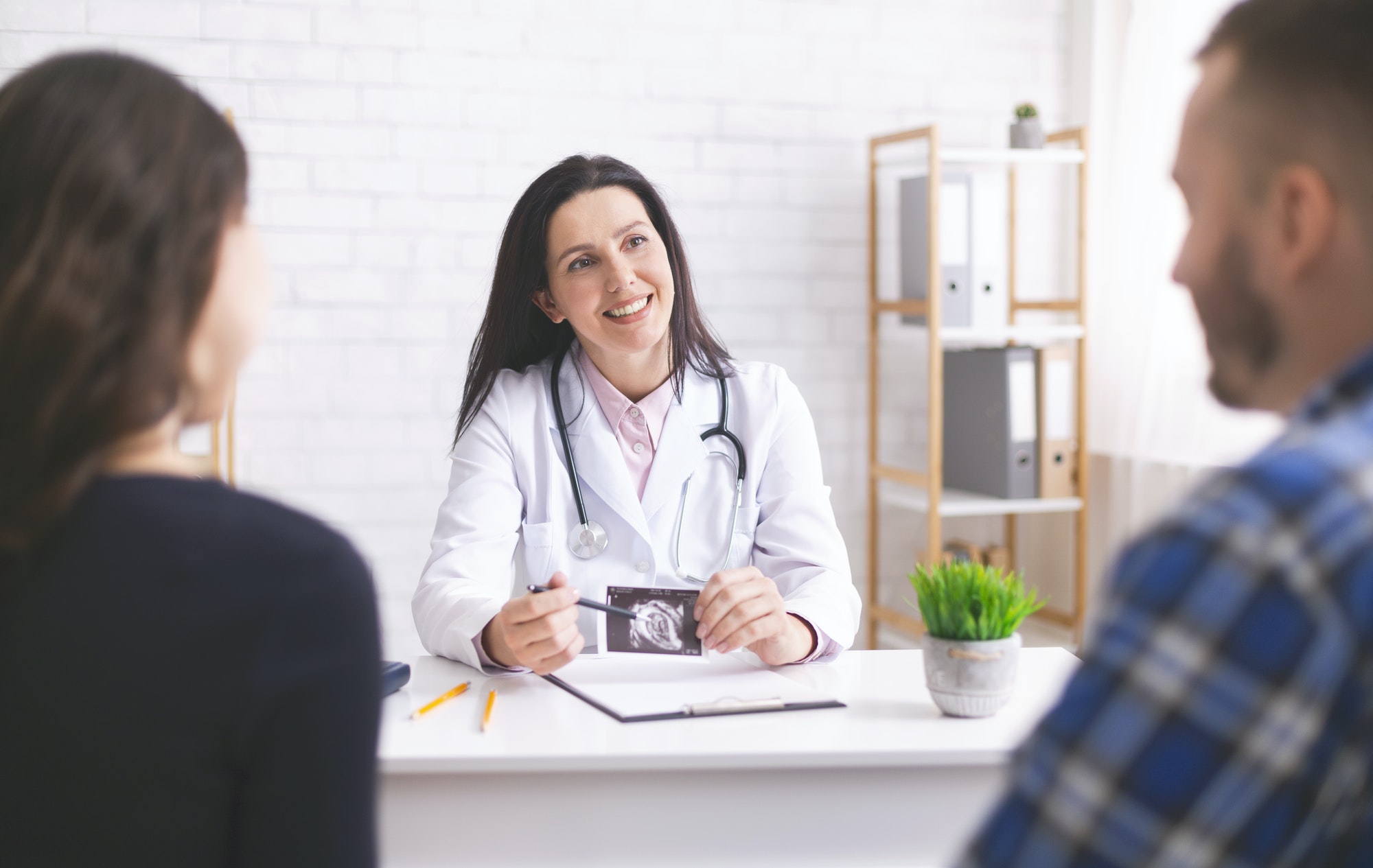 Friendly doctor explaining pregnancy diagnosis to young couple