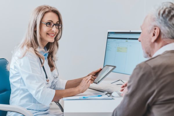 Friendly doctor talking with elderly man patient in the office using digital tablet
